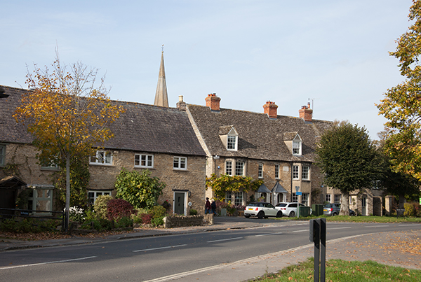 A panoramic view of a quaint village nestled in a misty valley, featuring green hills and a timeless church tower, creating a serene countryside atmosphere.