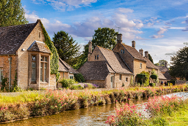 quaint stone cottages along a serene canal with blooming flowers and lush greenery under a blue sky